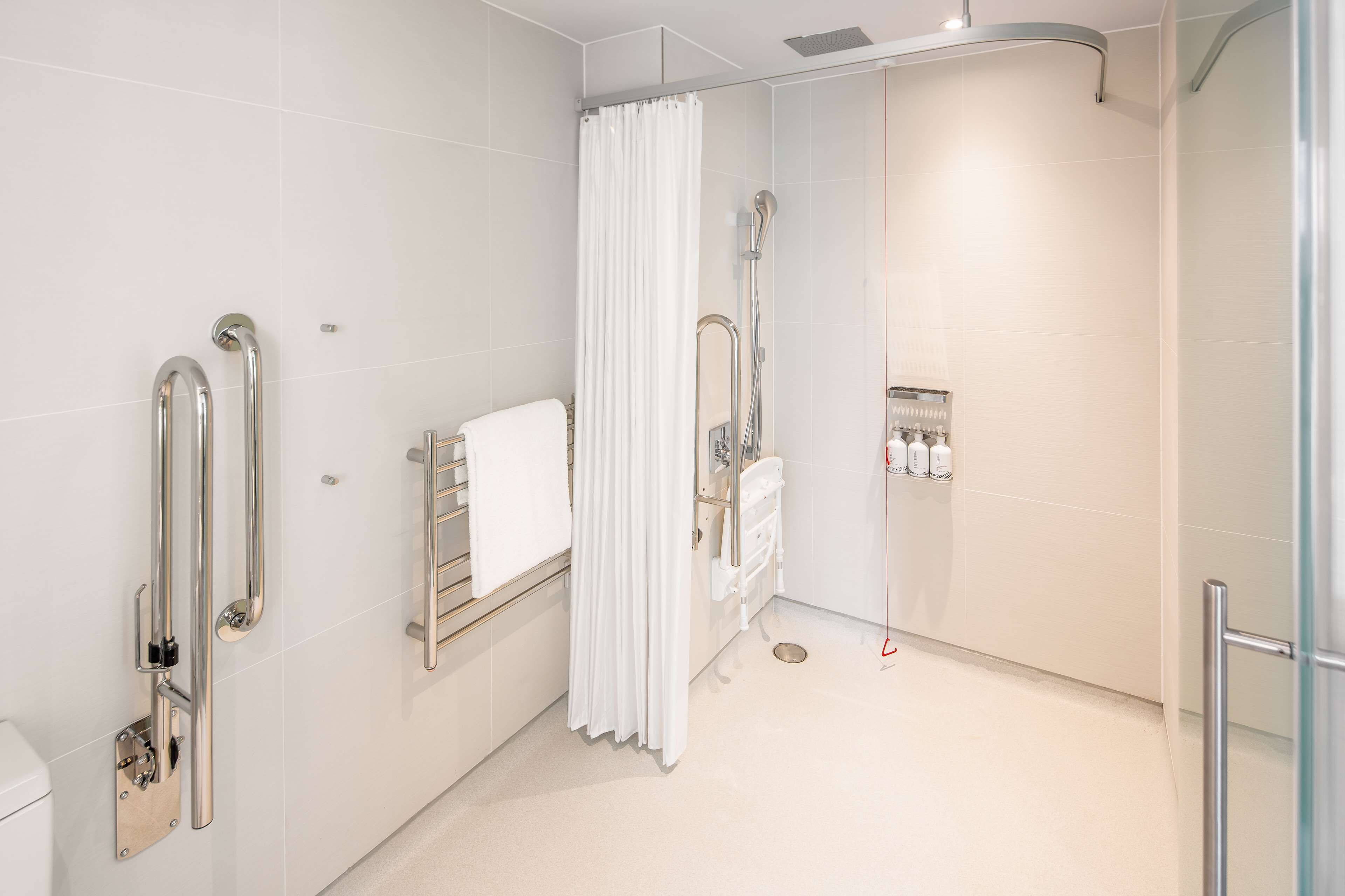 A modern bathroom with a walk-in shower, grab bars, a towel rack, and a glass partition.