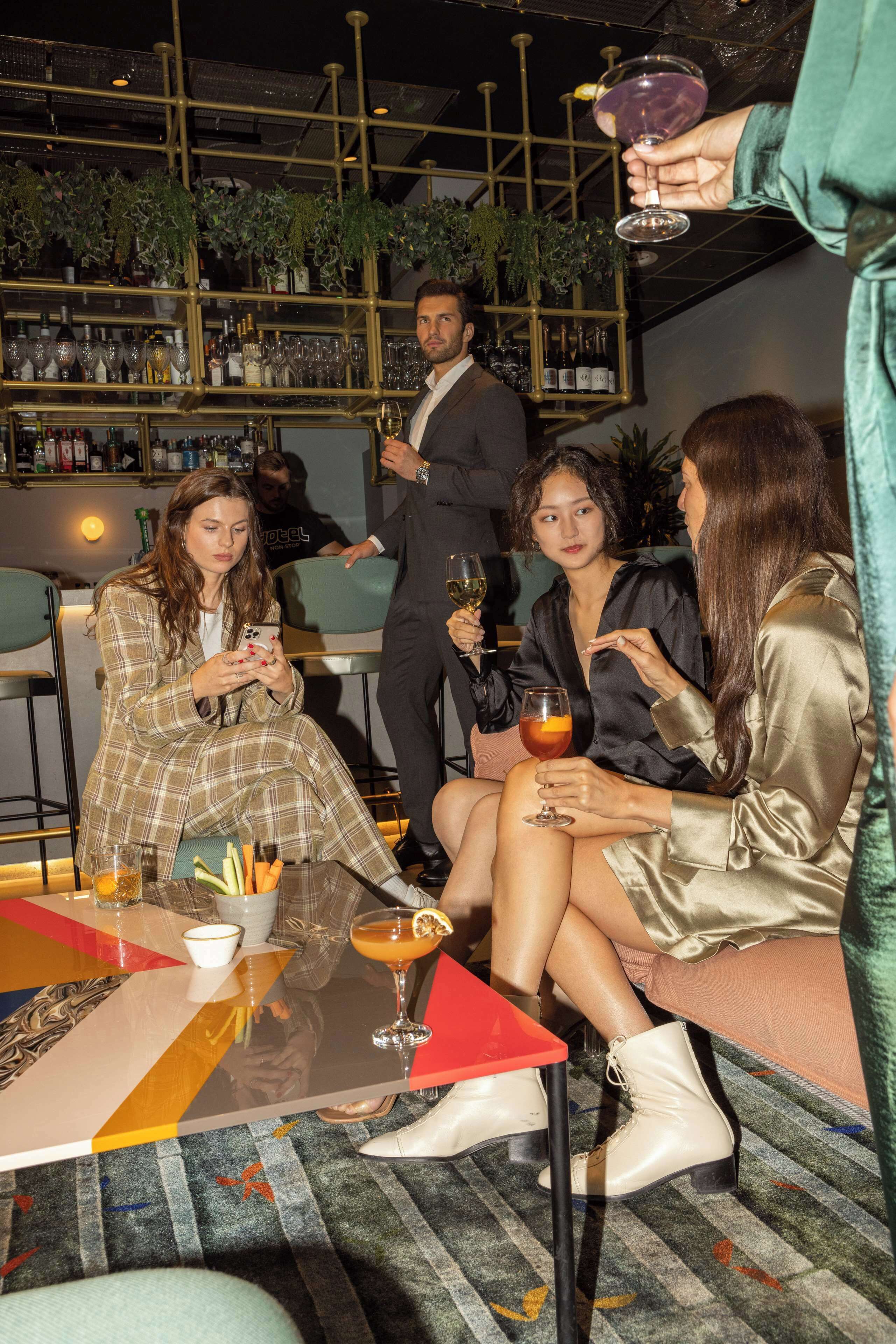 A group of people seated at a table with drinks, surrounded by shelves of bottles and glasses.