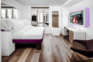 A modern hotel room with a bed, a desk, a chair, a TV, and a wardrobe.