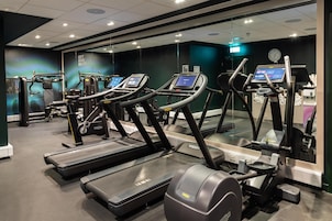 Ein Fitnessstudio mit Laufbändern, Trainingsgeräten und einer Spiegelwand.