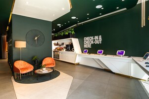A modern reception area with a check-in counter, two orange chairs, a lamp, and a clock on the wall.