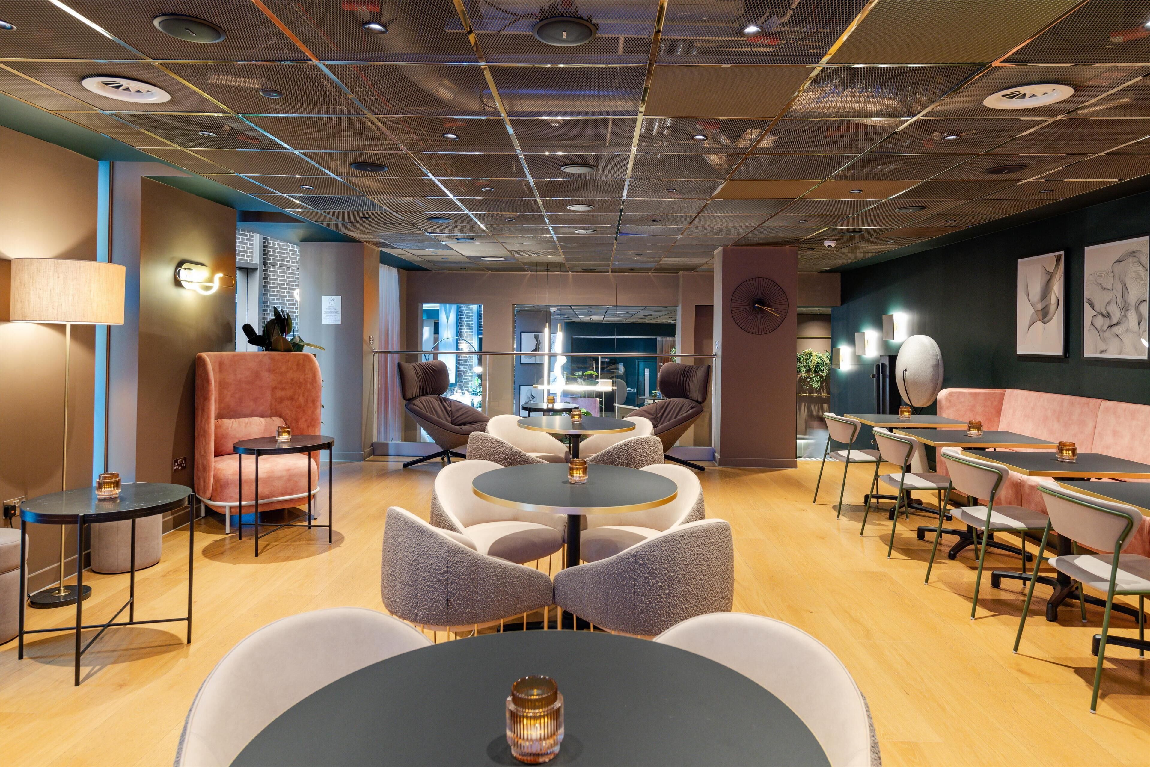 Un espace lounge moderne avec des tables rondes et des sièges confortables, agrémenté d’un plafond à motifs et offrant une vue sur le paysage urbain grâce à de grandes fenêtres.