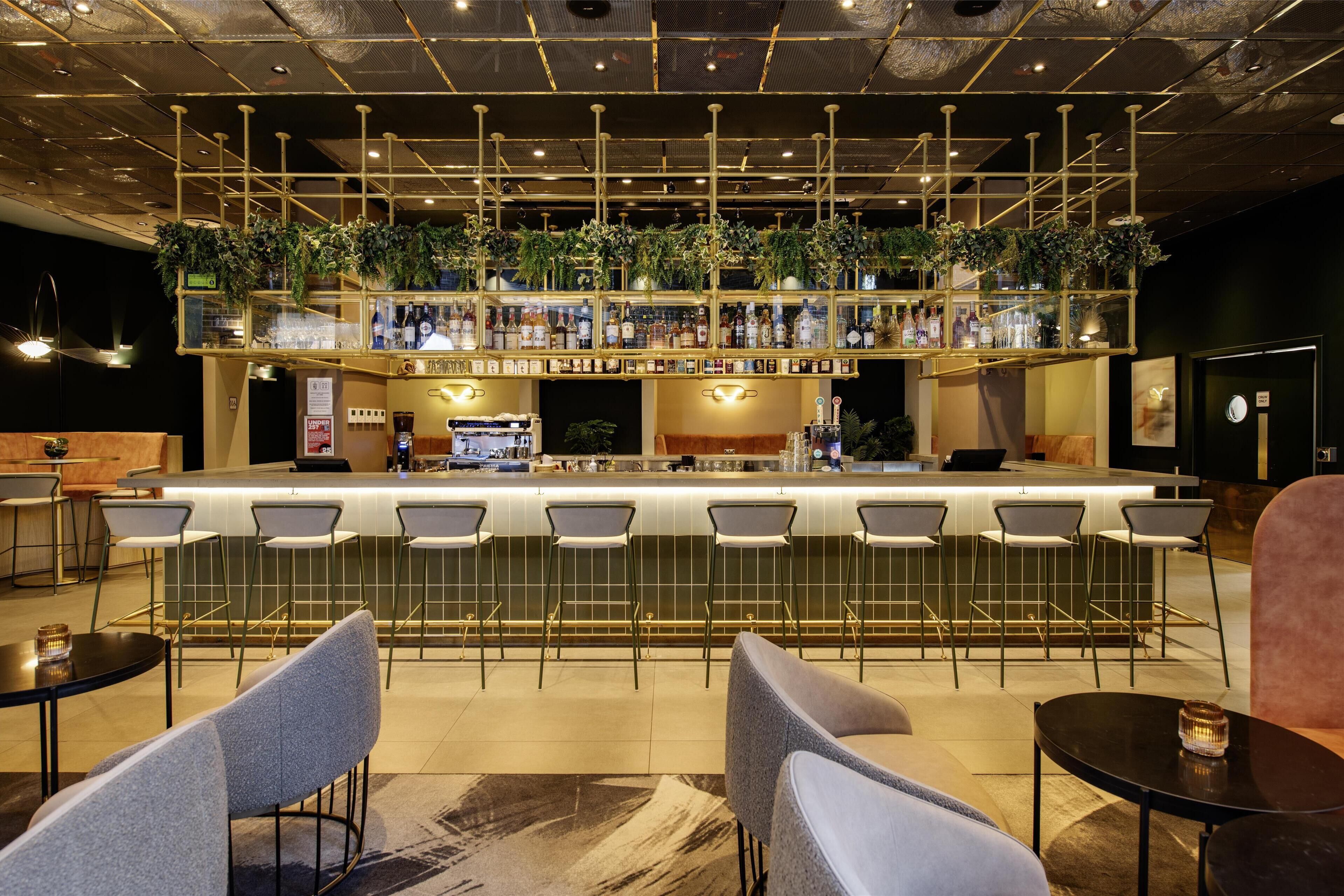 A bar area with multiple seating options, a counter with a variety of bottles, and a ceiling with exposed ductwork.
