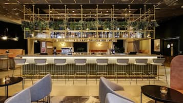 A bar area with multiple seating options, a counter with a variety of bottles, and a ceiling with exposed ductwork.