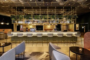 Eine Bar mit verschiedenen Sitzgelegenheiten, einer Theke voller Flaschen und einer Decke mit freiliegenden Lüftungsrohren.