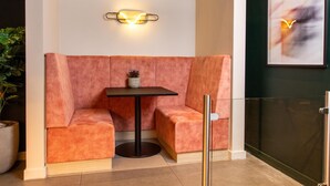 A seating area with a table, cushioned benches, a wall-mounted light fixture, and a framed abstract painting. - Yotel London City (London)