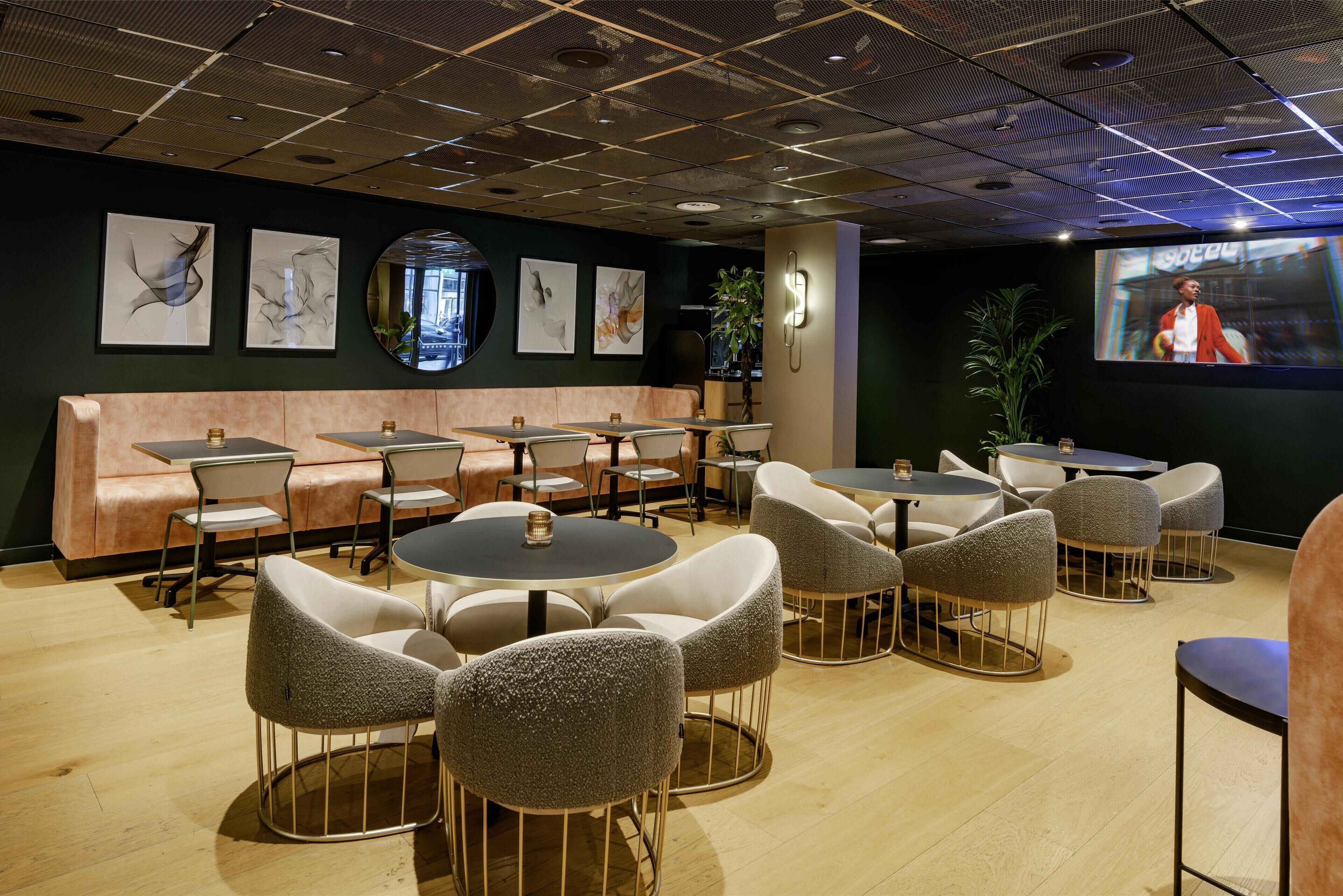 Un restaurante moderno con mesas redondas y sillas acolchadas, una barra con caja registradora y obras de arte en las paredes.