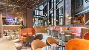 A modern interior with a mix of seating areas, including sofas and chairs, and a bar area with a staircase. - Yotel London City (London)