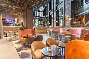Un interior moderno con varios rincones de estar, incluyendo sofás y sillones, y una zona de bar con una escalera.