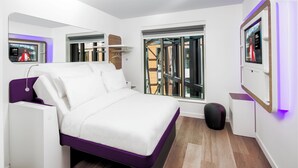 A modern bedroom with a bed, a small seating area, a TV, and a window with a view of the outside. - Yotel London City (London)
