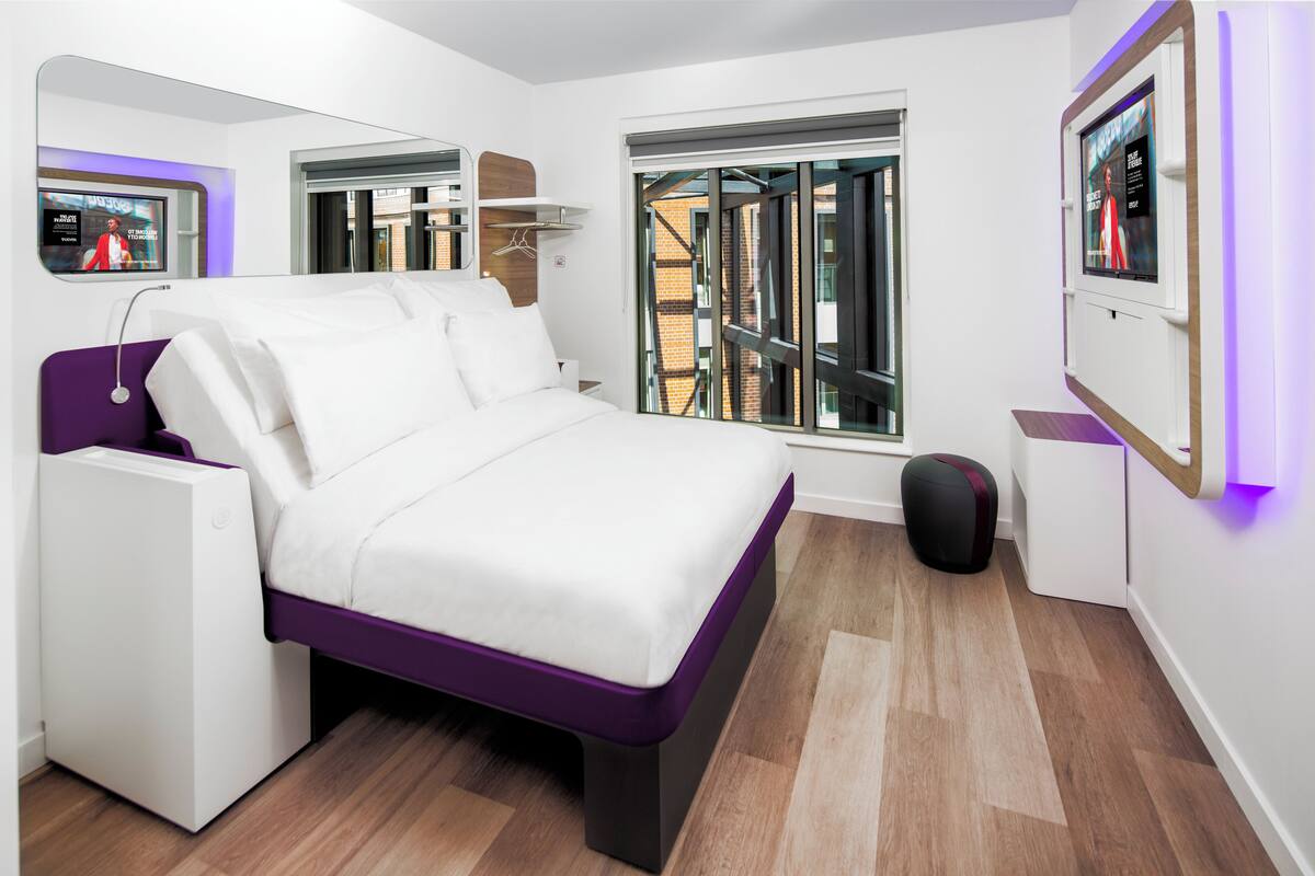A modern bedroom with a bed, a small seating area, a TV, and a window with a view of the outside.