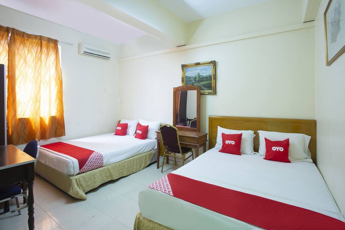 A hotel room with two single beds, a desk, a chair, and a mirror.