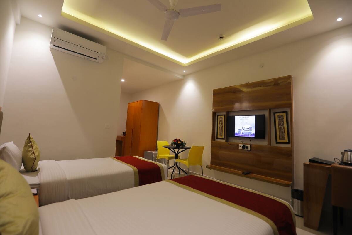 Habitación de hotel con dos camas, un escritorio, una silla, un televisor y un ventilador de techo.