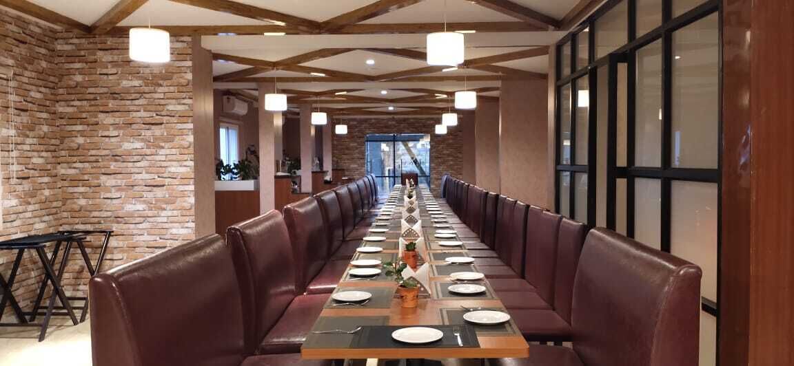A long dining table with leather booths, a brick wall, and pendant lighting.