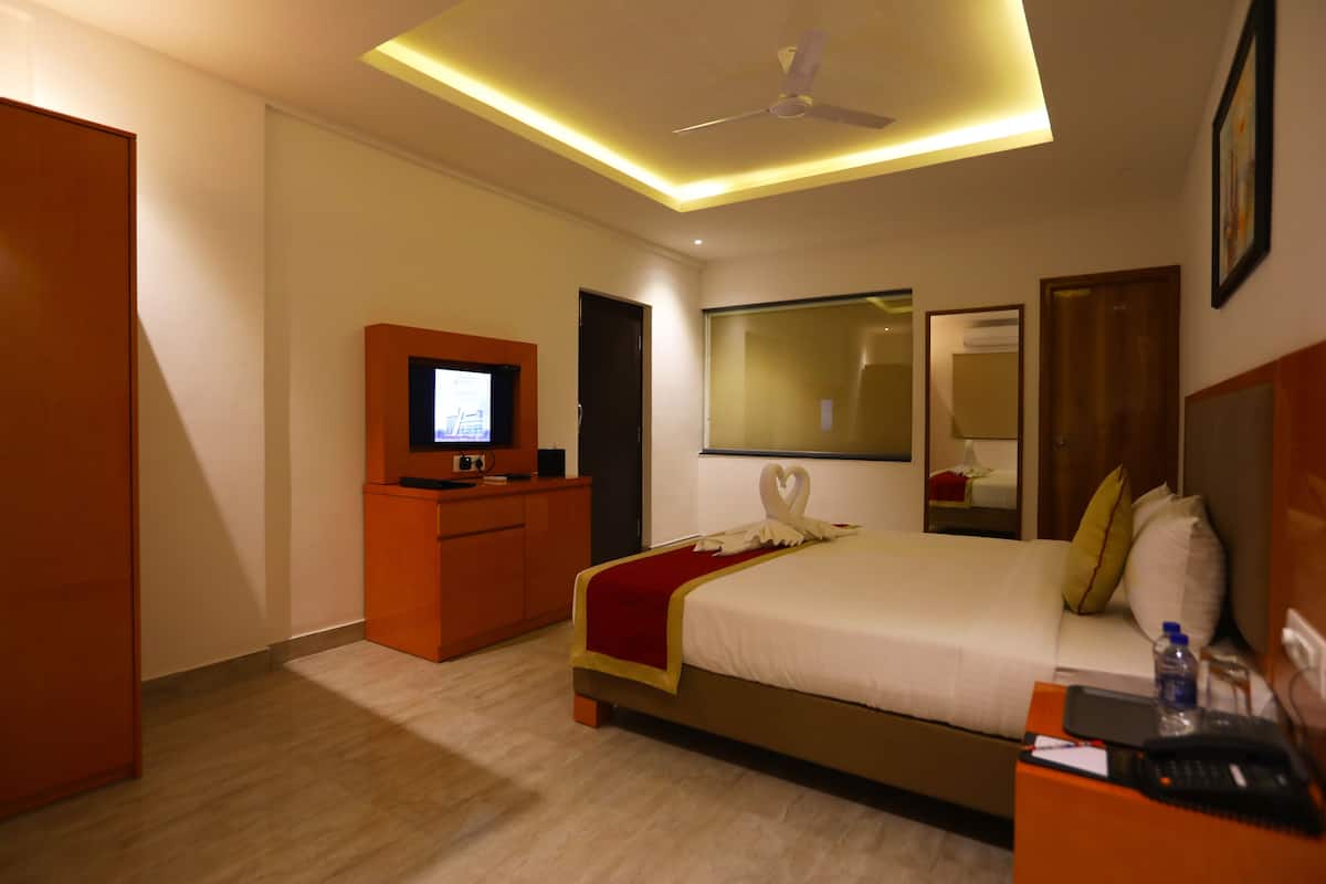 Habitación de hotel con cama, escritorio, televisor, ventilador de techo y espejo.