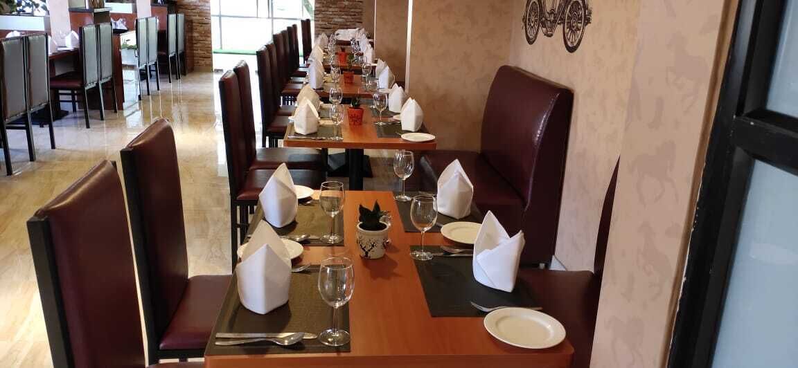 A restaurant with long tables set for dining, each with a place setting including a plate, glass, and napkin.