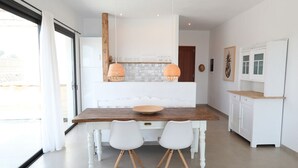 Comedor con mesa de madera, dos sillas blancas y un armario blanco con encimera de madera.