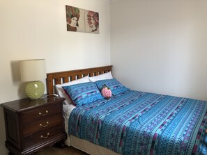 Une chambre à coucher avec un lit en bois, une table de chevet avec une lampe, une commode et deux tableaux accrochés au mur.