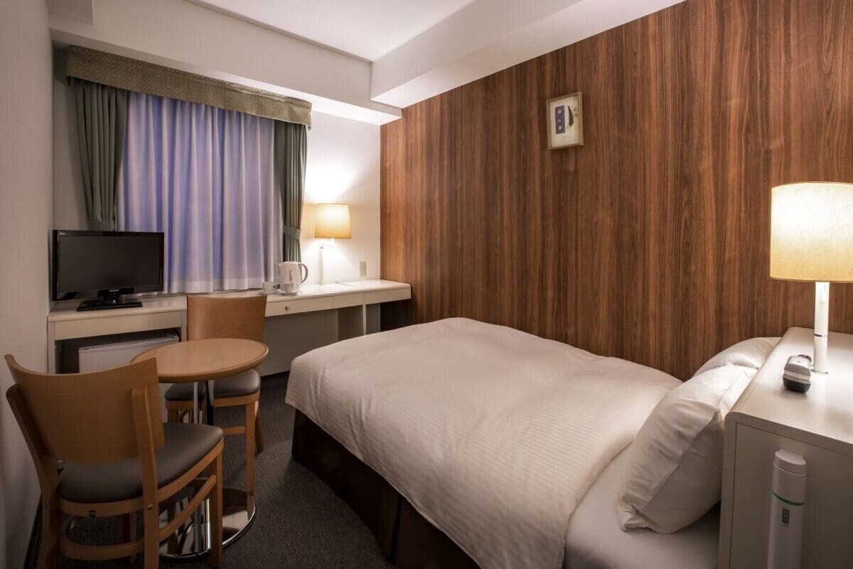 Une chambre d’hôtel équipée d’un lit, d’un bureau avec un ordinateur, d’une chaise, d’une lampe et d’un téléviseur.