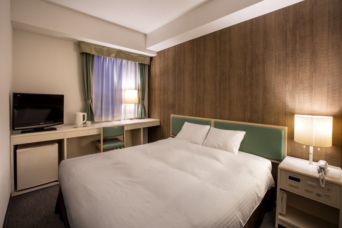 A hotel room with a bed, a desk with a television, a lamp, and a telephone.