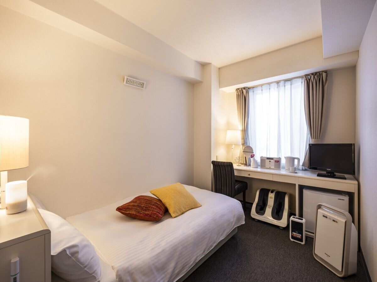 Une chambre d’hôtel équipée d’un lit, d’un bureau, d’une chaise, d’un ordinateur et d’un petit radiateur.