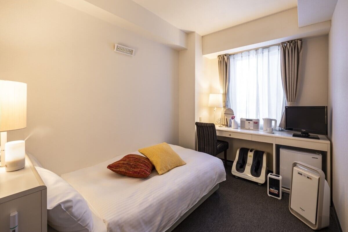 Une chambre d’hôtel équipée d’un lit, d’un bureau, d’une chaise, d’un ordinateur et d’un petit radiateur.