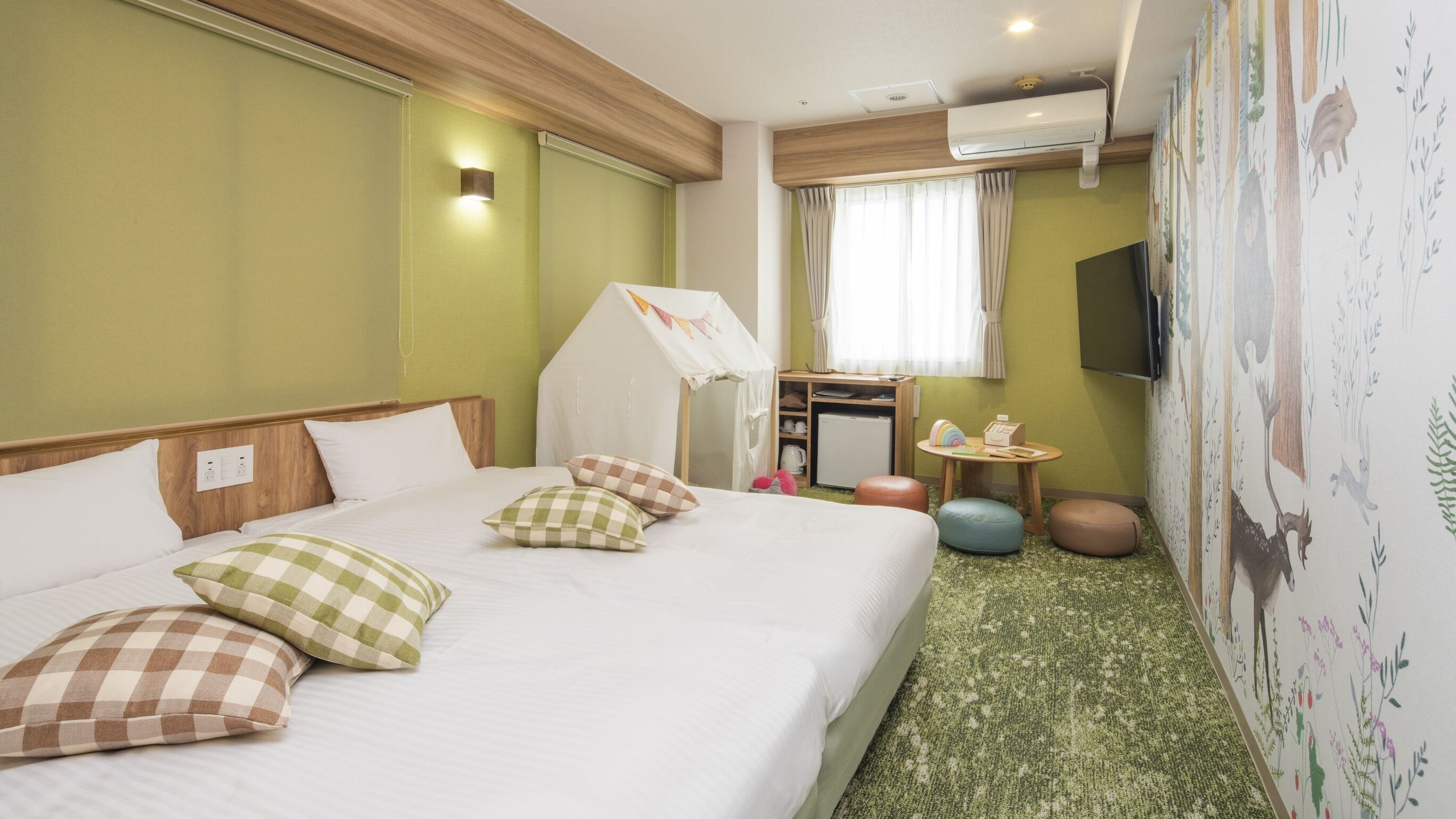 Habitación de hotel con cama, una mesita, un espejo, televisor y una pared decorada con un mural de temática natural.
