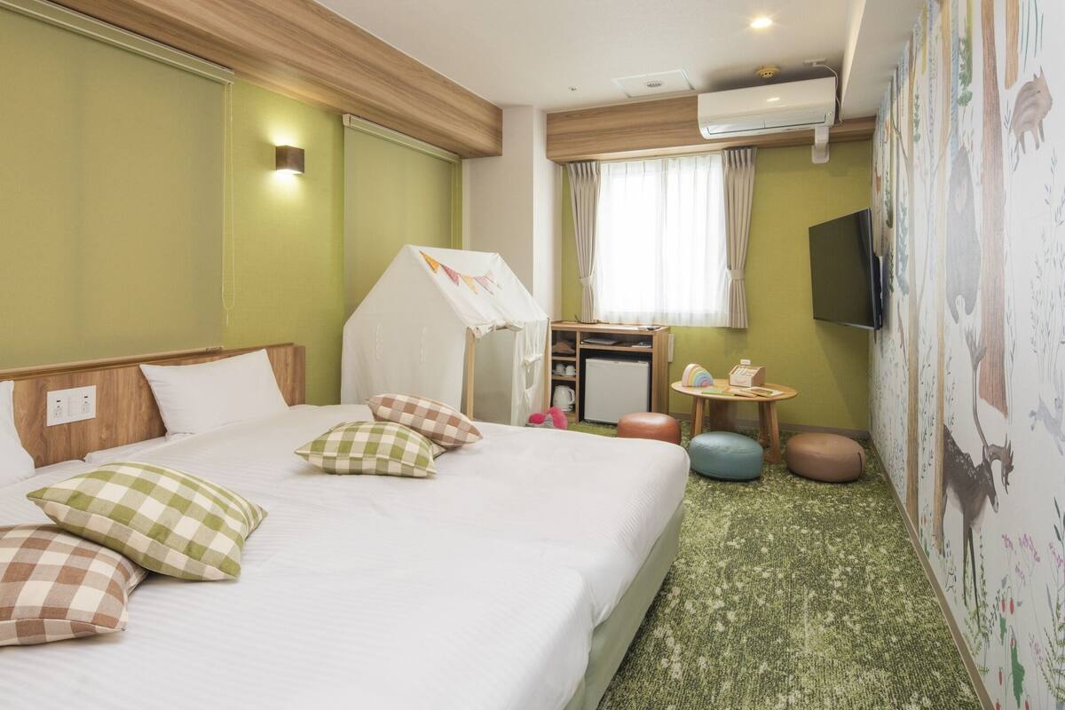 Une chambre d’hôtel comprenant un lit, une petite table, un miroir, un téléviseur et un mur orné d’une fresque sur le thème de la nature.
