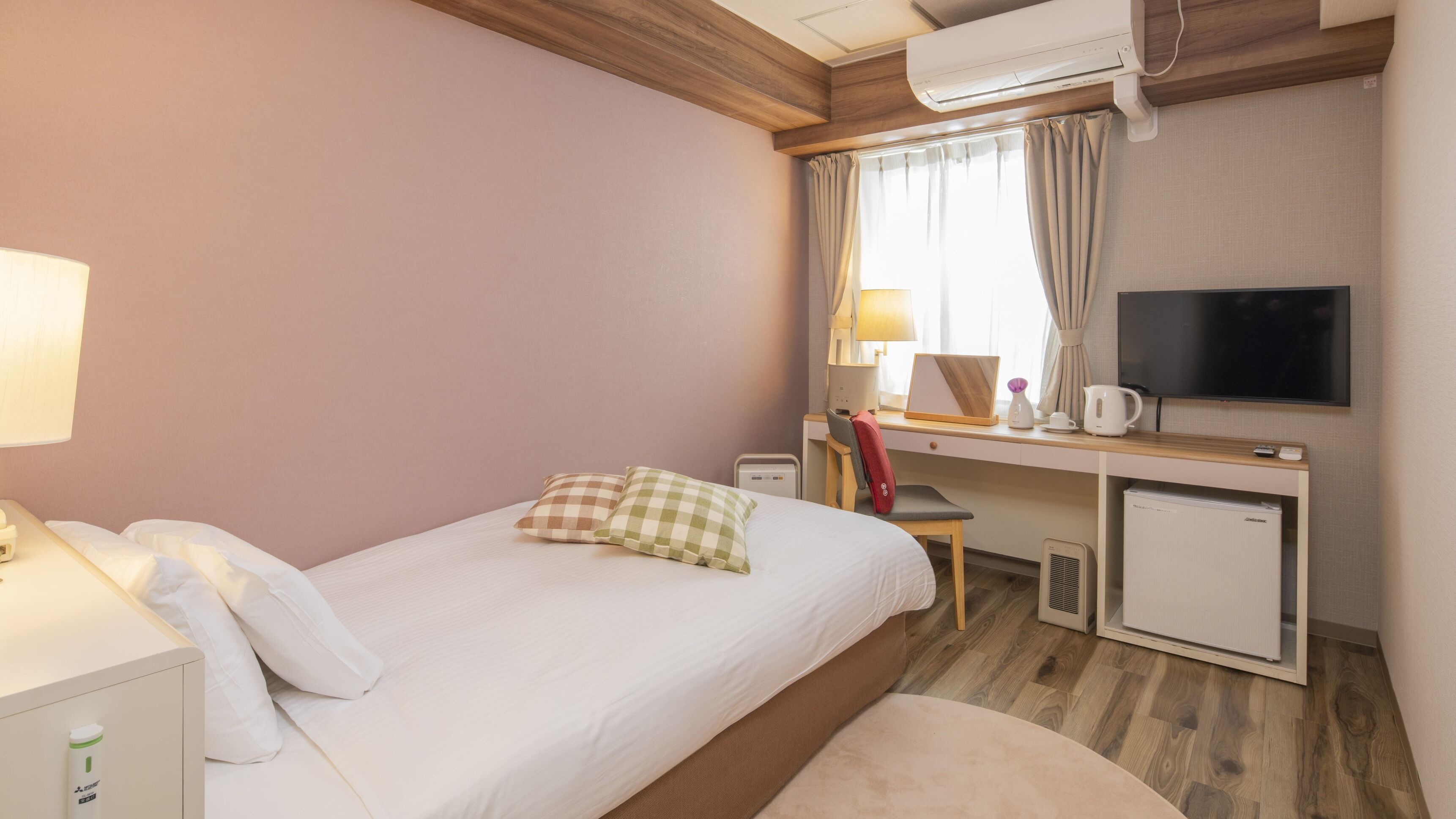 Habitación de hotel con cama, escritorio con computadora, televisión y refrigerador pequeño.