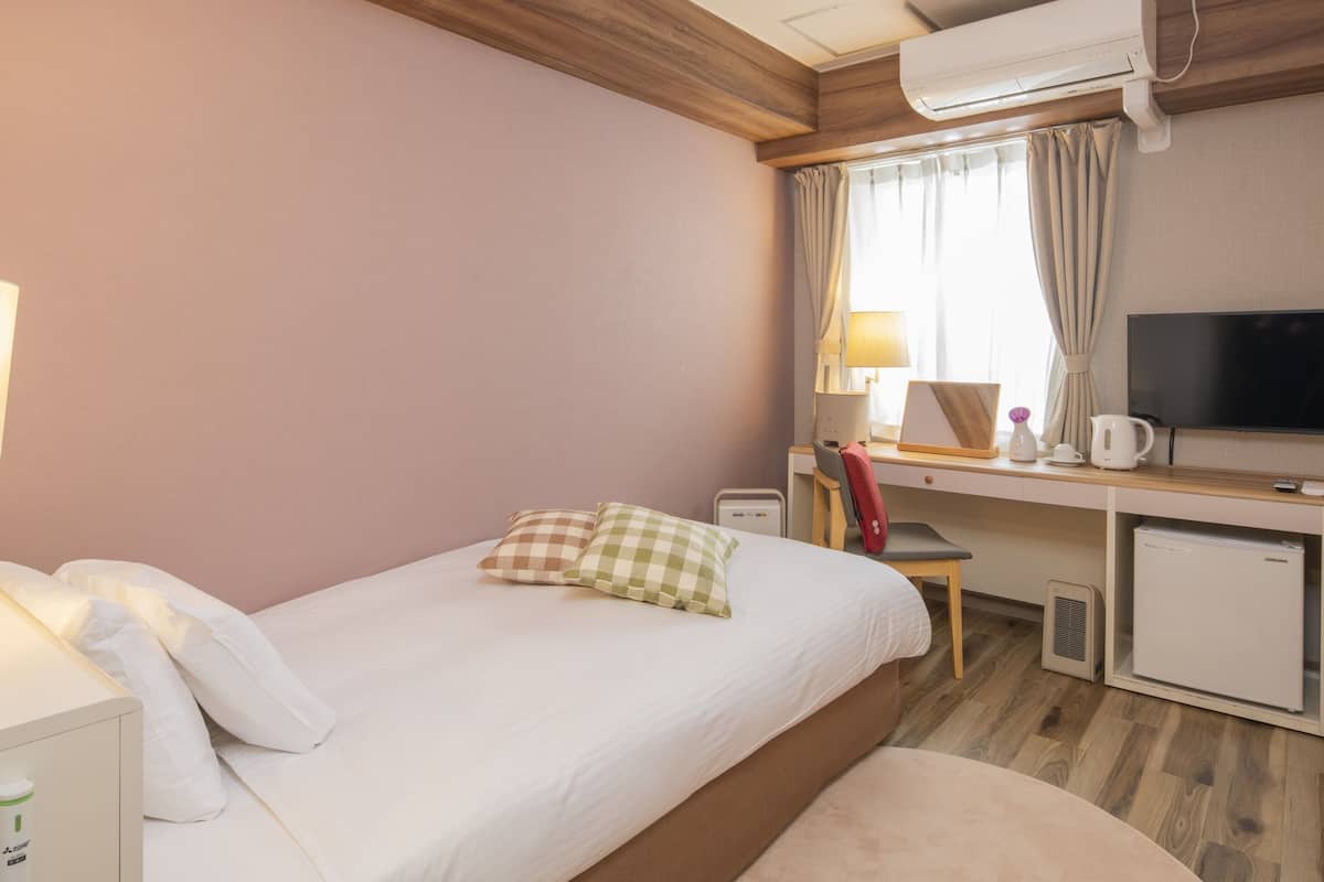 Une chambre d’hôtel équipée d’un lit, d’un bureau avec un ordinateur, d’une télévision et d’un mini-réfrigérateur.