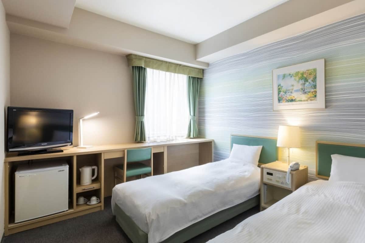 Une chambre d’hôtel avec deux lits, une télévision, un bureau et un tableau au mur.