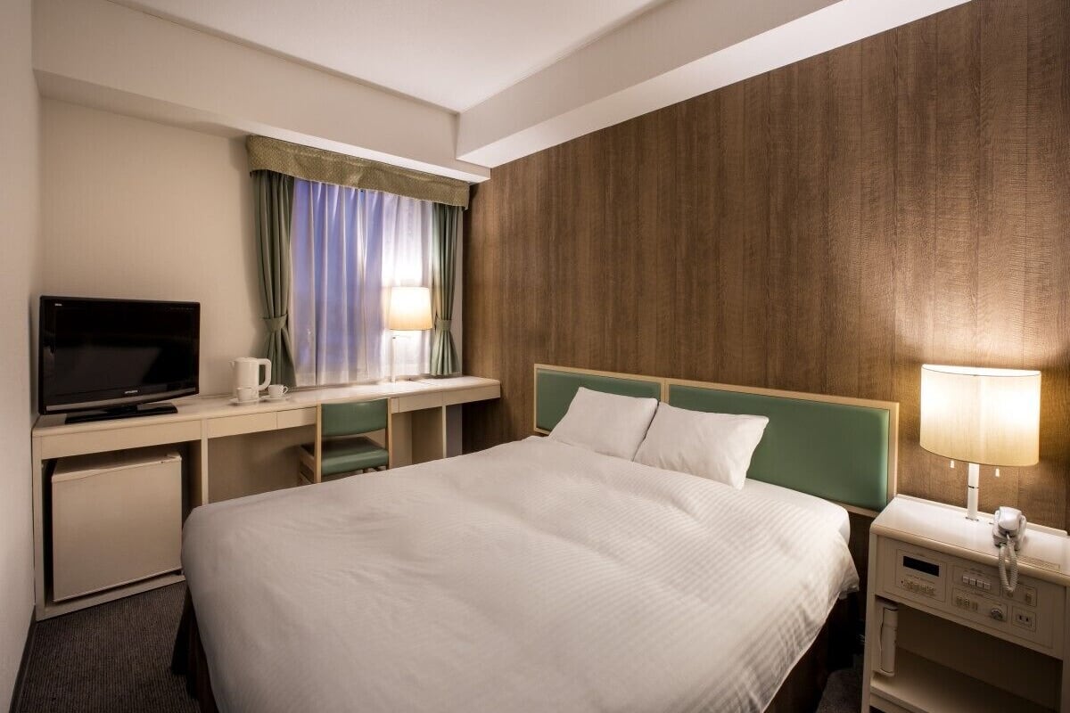 Une chambre d’hôtel comprenant un lit, un bureau avec une télévision, une lampe et un téléphone.