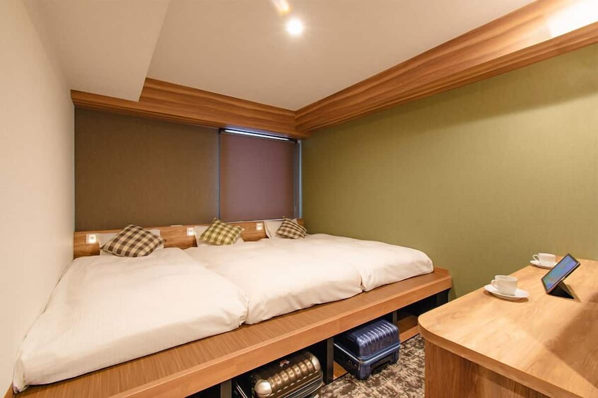 Une chambre d’hôtel avec un lit double, une table de chevet avec une tasse et une tablette, et une fenêtre avec des stores.