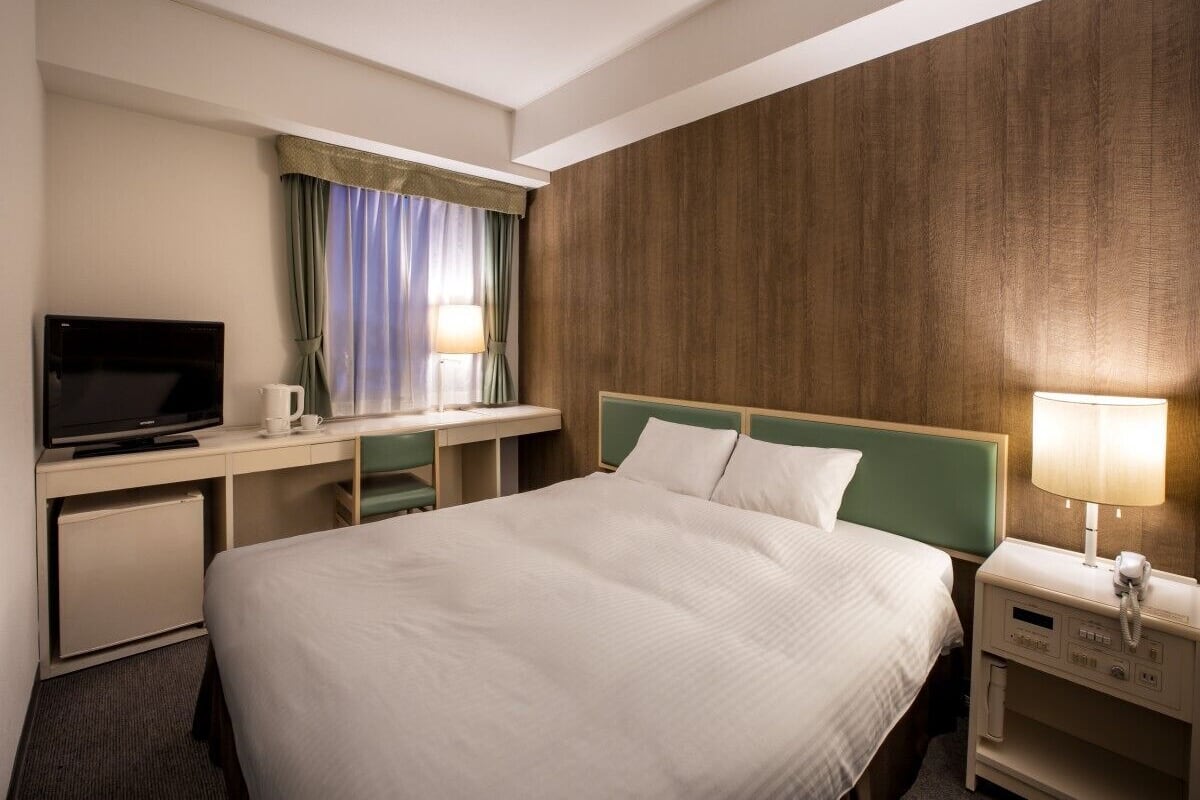 Une chambre d’hôtel comprenant un lit, un bureau avec une télévision, une lampe et un téléphone.