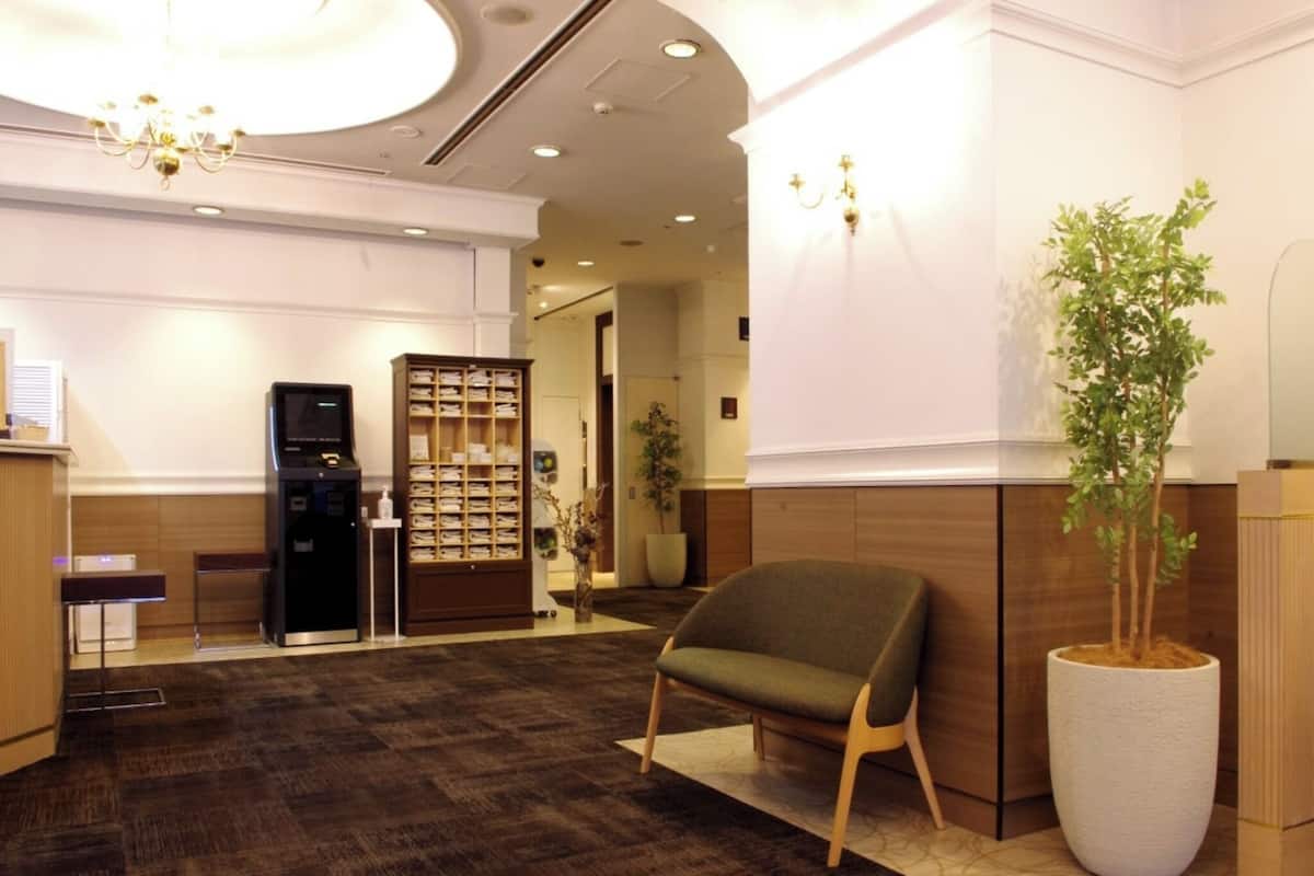 Un espace d’accueil avec un tapis foncé, un comptoir de réception, une grande plante en pot et une bibliothèque en bois.