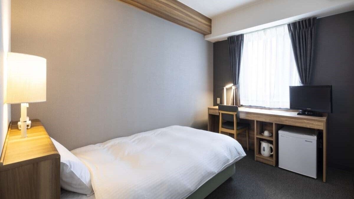 Una habitación de hotel con cama, escritorio, computadora, televisor y refrigerador pequeño.