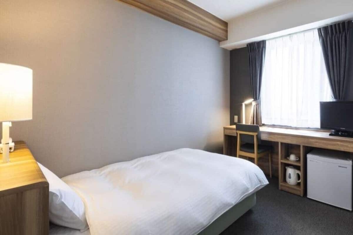 Une chambre d’hôtel équipée d’un lit, d’un bureau avec un ordinateur, d’une télévision et d’un mini-réfrigérateur.