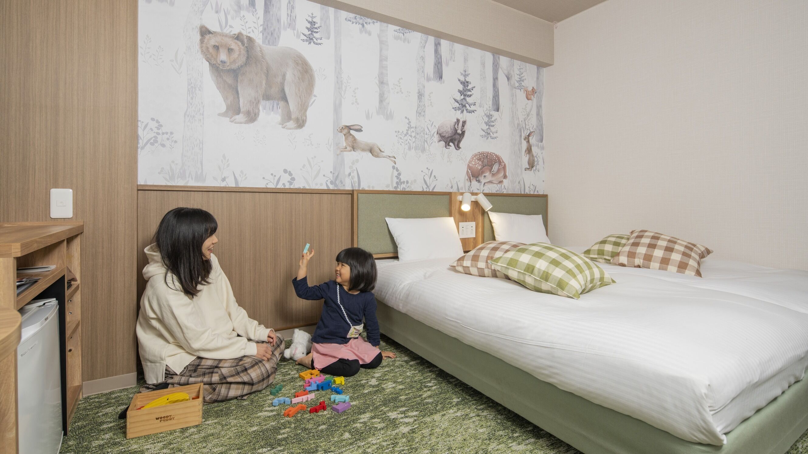 Un dormitorio con una cama, una mesita de noche, un papel tapiz con motivos forestales y un armario de madera.