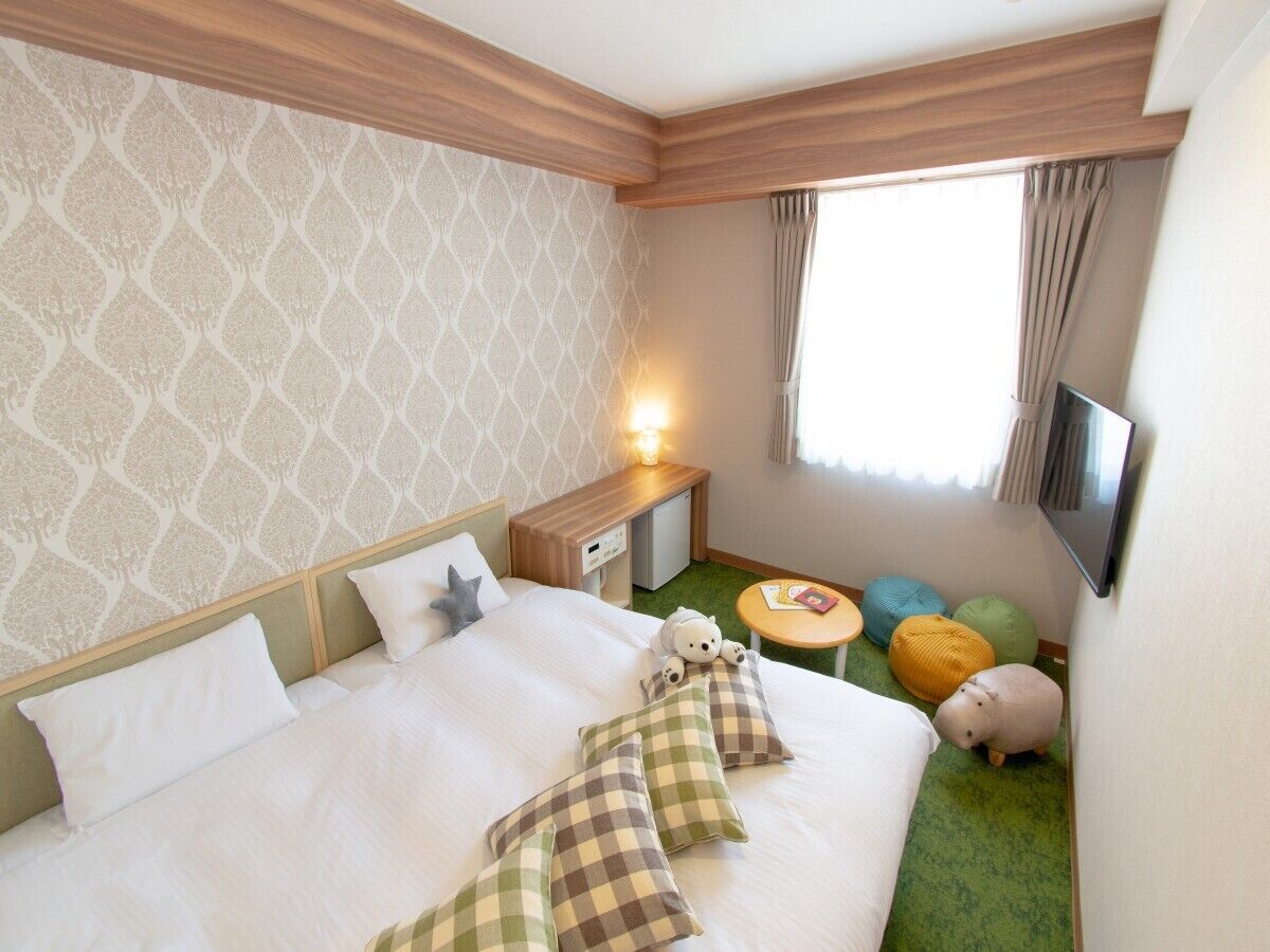 Una habitación de hotel con una cama grande, una mesita de noche, un televisor y una pequeña mesa con cojines de colores.