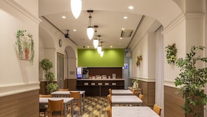 Ein Restaurant mit Marmortischen, Holzstühlen, einer grünen Akzentwand und hängenden Pendelleuchten.