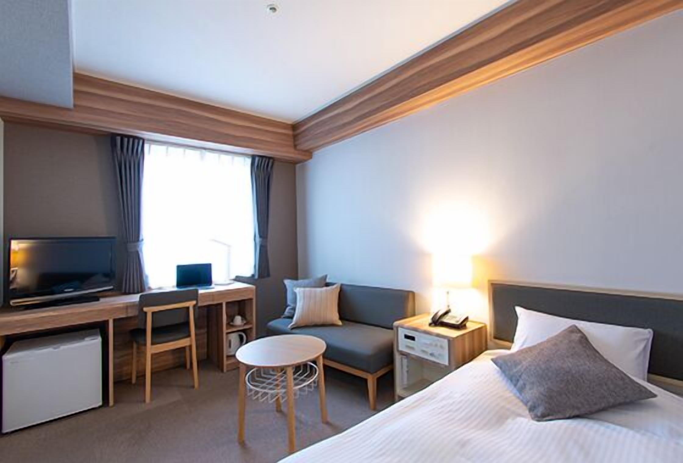 Une chambre d’hôtel comprenant un lit, un bureau avec un ordinateur, une télévision, une petite table et un canapé.