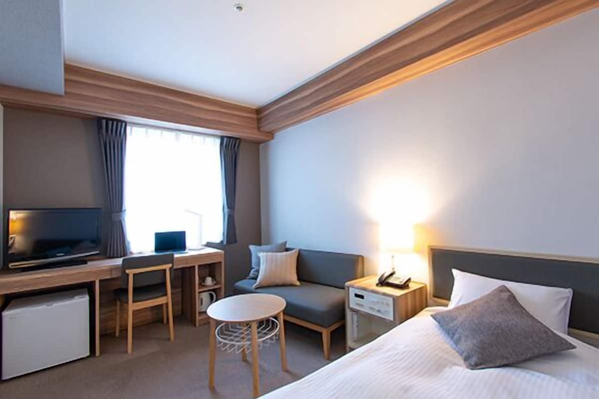 Une chambre d’hôtel comprenant un lit, un bureau avec un ordinateur, une télévision, une petite table et un canapé.