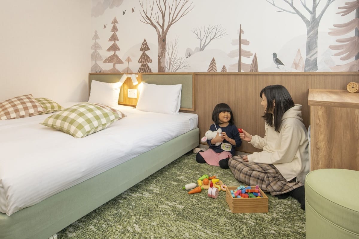 Une chambre à coucher avec un lit, des oreillers, une table de chevet, une tête de lit en bois, une fresque murale, une horloge et une boîte à jouets.