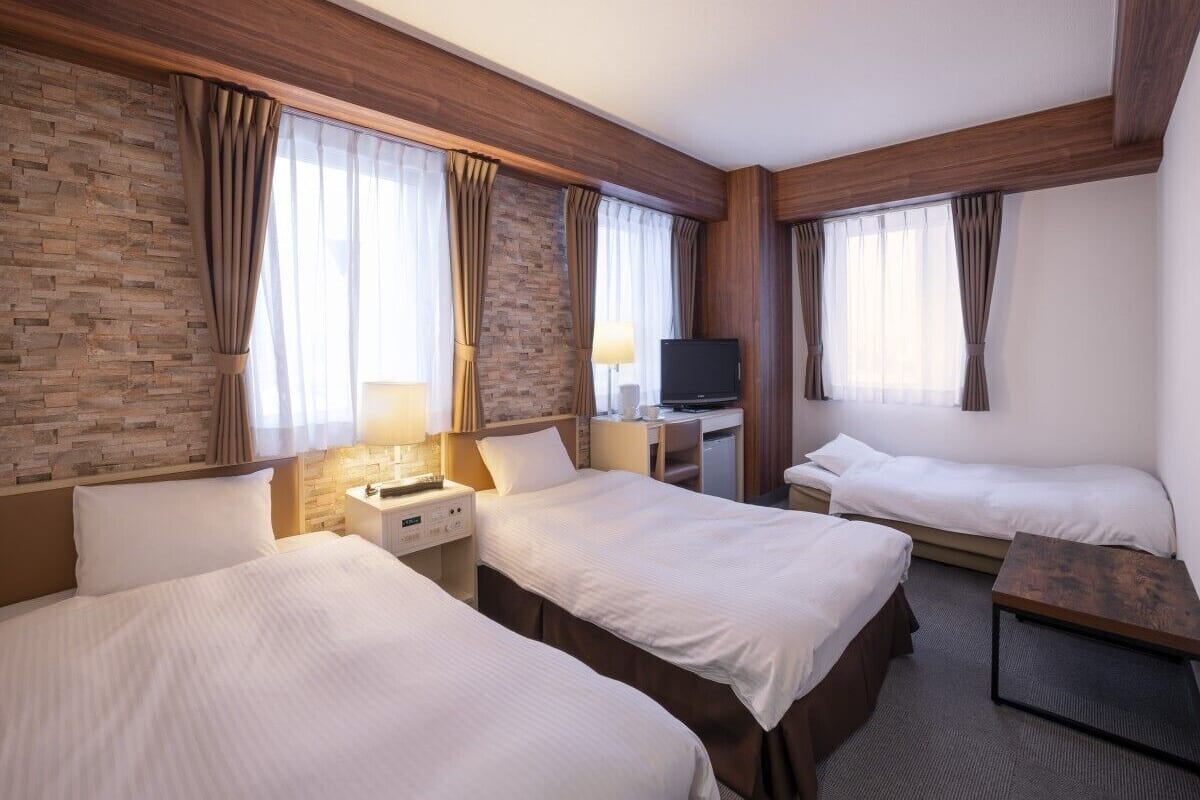 Une chambre d’hôtel avec trois lits, une télévision, un bureau et une lampe.