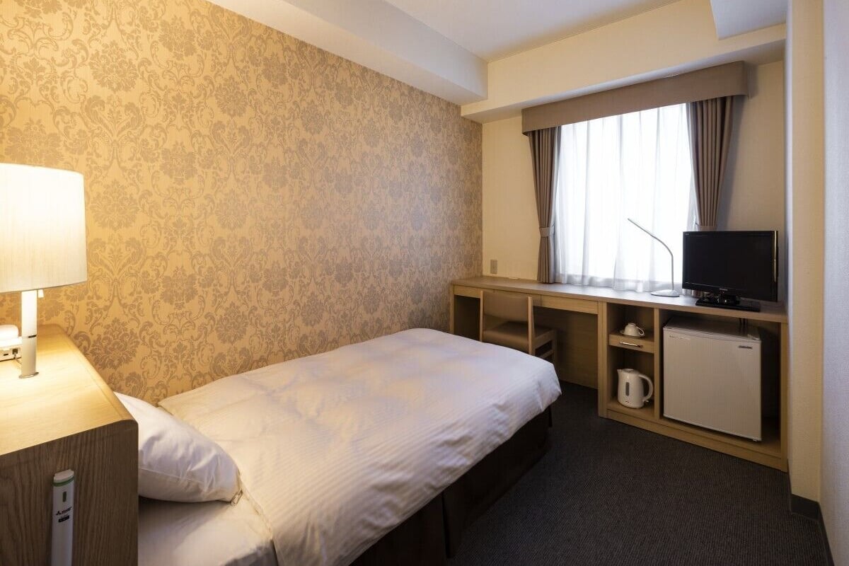 Une chambre d’hôtel équipée d’un lit, d’un bureau, d  ’une télévision et d’un petit réfrigérateur.