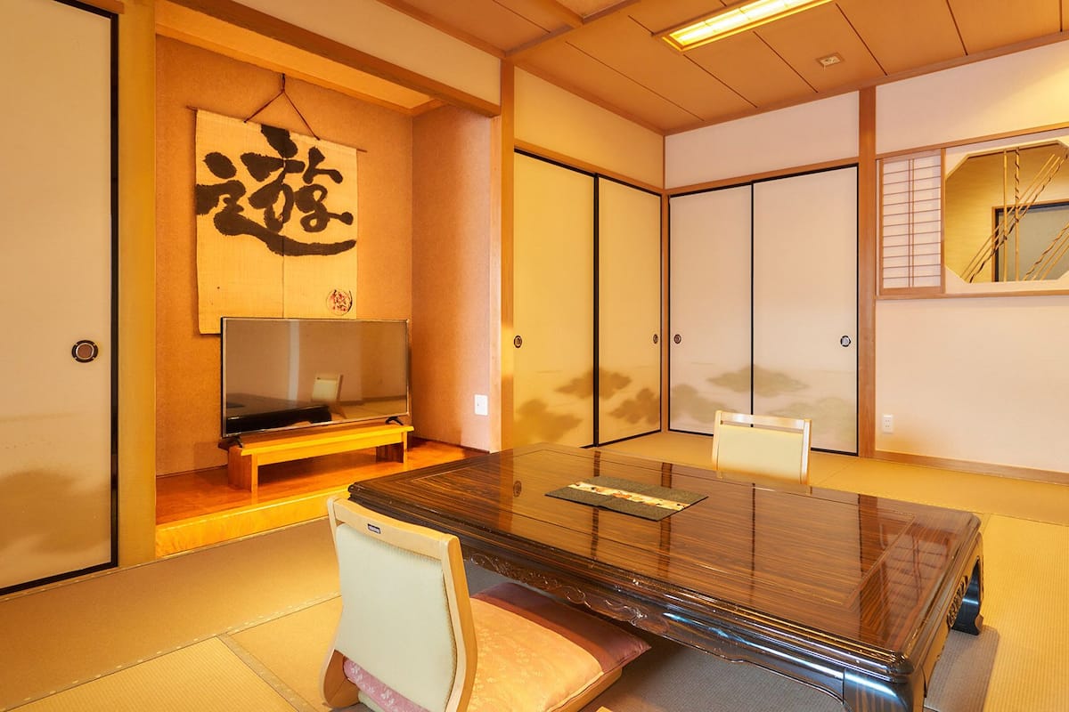 Ein traditioneller japanischer Raum mit Tatami-Böden, einem niedrigen Tisch, einem Fernseher, Schiebetüren und einem Shoji-Bildschirm.