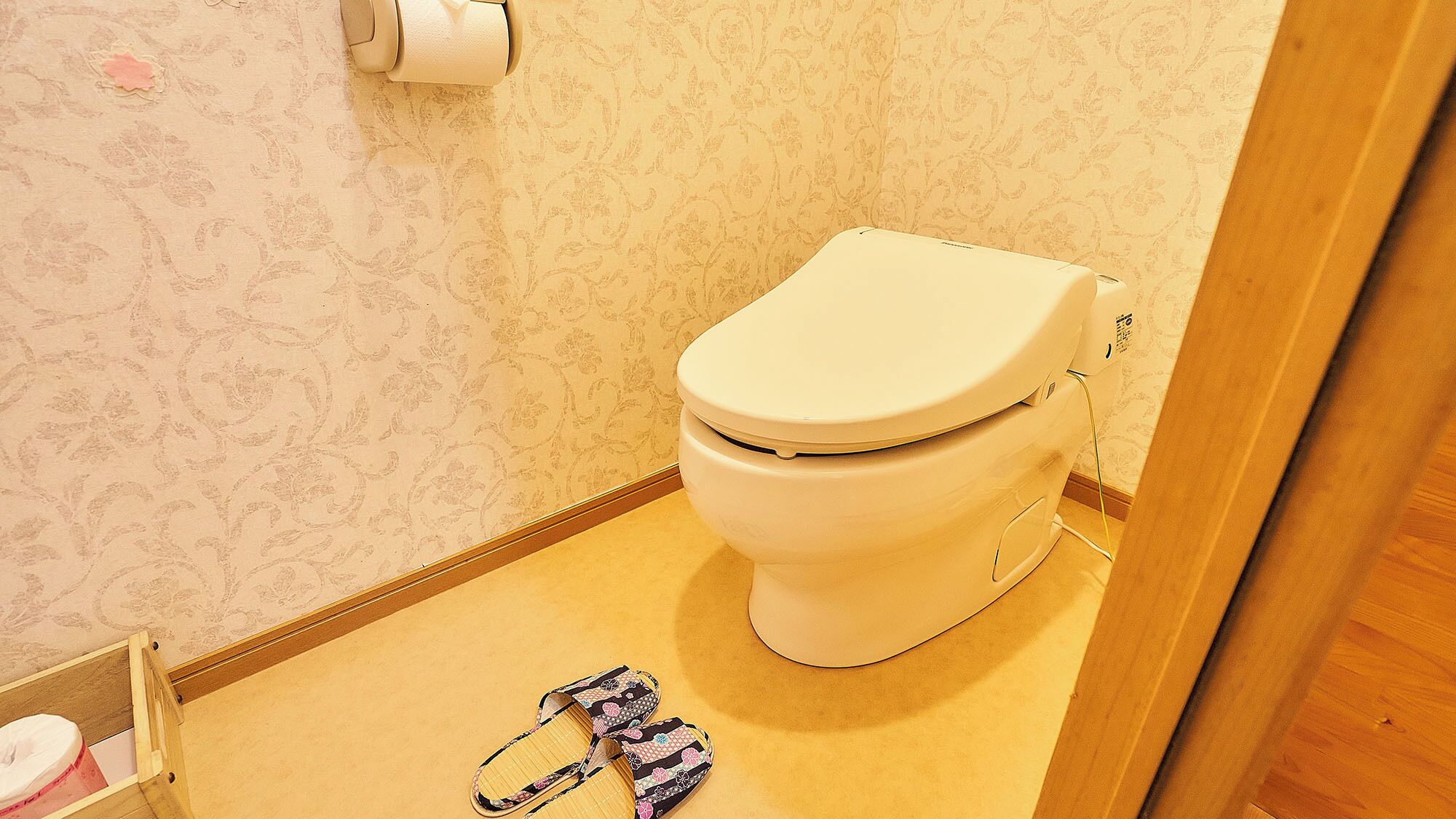 Kylpyhuoneessa on wc, rulla wc-paperia ja parin tohvelit lattialla.