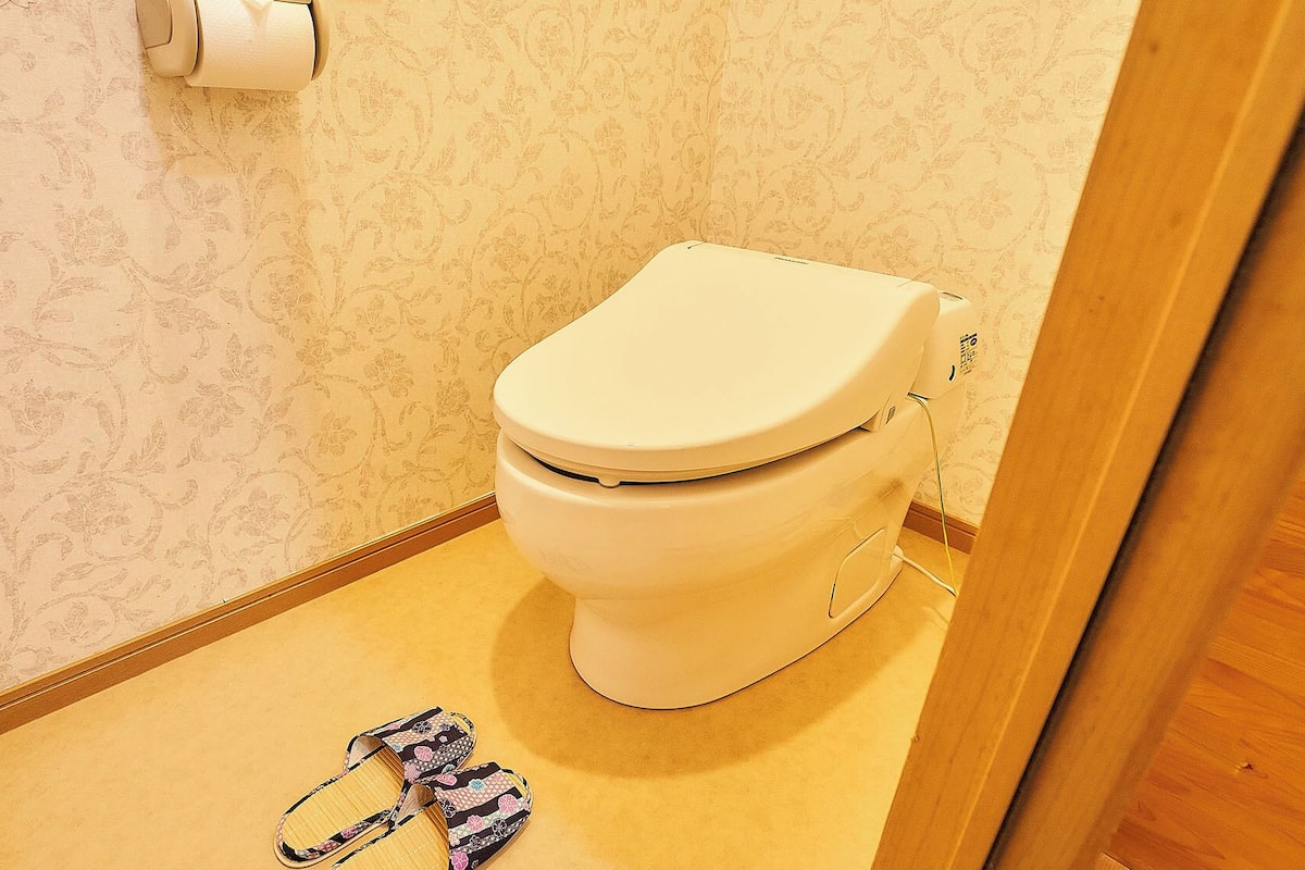 Ein Badezimmer mit Toilette, Toilettenpapier und einem Paar Hausschuhen auf dem Boden.
