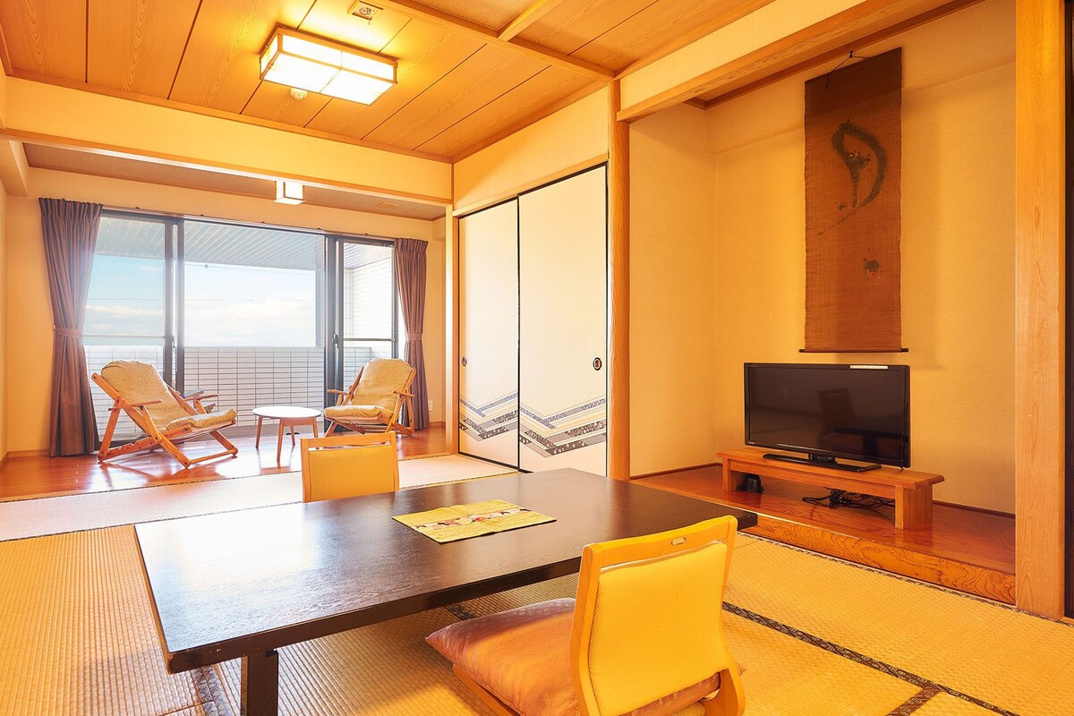 Une pièce avec un plancher en bois, un tatami, une télévision et deux chaises.