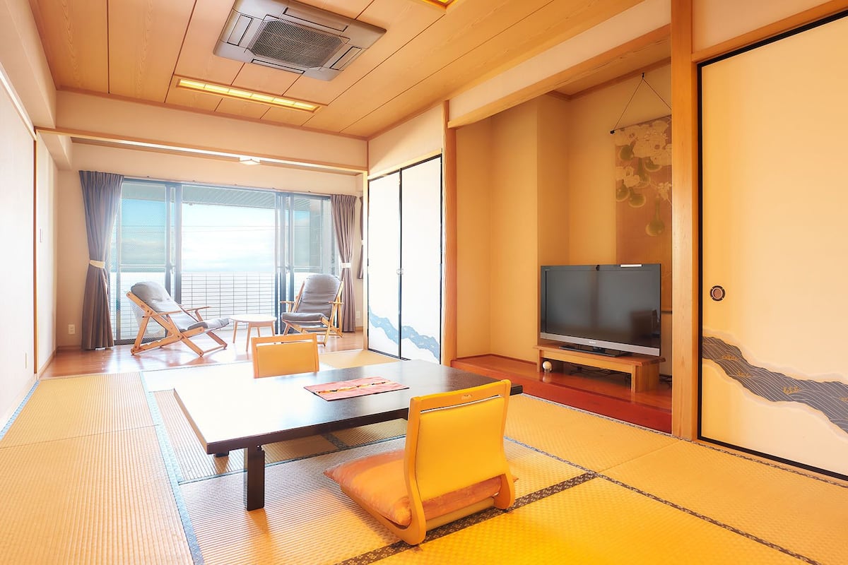 Ein Hotelzimmer mit einer großen Schiebeglasdoor, einem Flachbildfernseher, einem Boden mit Tatami-Matten und einer traditionellen japanischen Schiebetür.